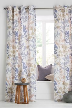 a window with curtains and pillows on the floor next to a stool in front of it