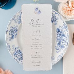 a blue and white plate with a menu card on it next to some pink flowers