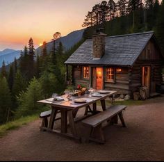 a picnic table set up in front of a log cabin with the sun setting behind it