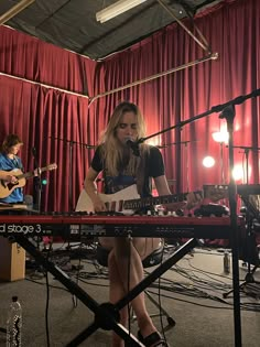 a woman sitting on top of a keyboard in front of a microphone and guitar player