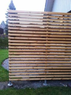 a wooden slatted fence in front of a house with grass and trees around it