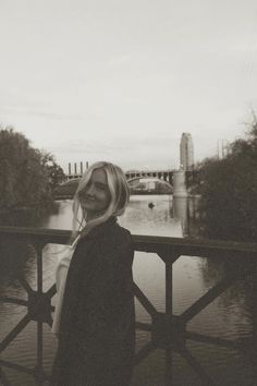 a woman standing on a bridge next to a river with a bridge in the background