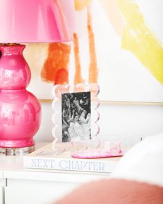 a pink lamp sitting on top of a white table next to a book and photo