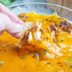 a hand holding a piece of bread over a bowl filled with cheese and other food