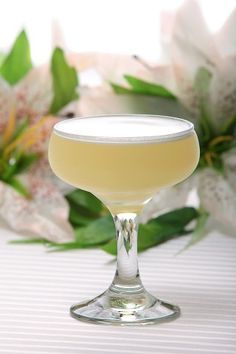 a glass filled with a drink sitting on top of a table next to white flowers