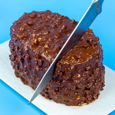 a knife cutting into a chocolate cake on top of a white plate with blue background