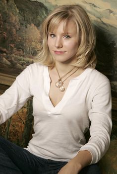 a woman sitting in front of a painting wearing a white shirt and blue jeans with her hands on her hips