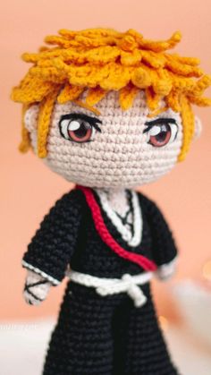 a crocheted doll with blonde hair and red eyes wearing a black dress, standing on a white surface