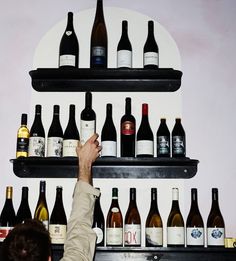 a man is reaching up to the shelves with wine bottles on it and he is pointing at them