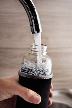 a person is pouring water from a faucet into a glass jar with gravel inside