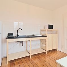 an empty kitchen with wooden floors and white tiles on the walls, along with a black counter top