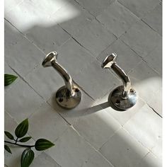 two metal handles on the side of a white tile floor next to a green plant