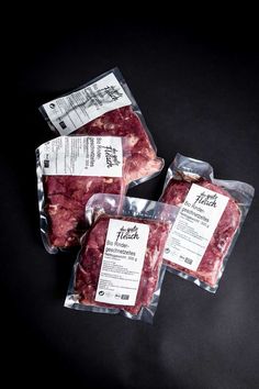 three packages of meat sitting on top of a black table next to eachother