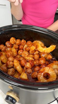 a woman is cooking some food in the slow cooker and it looks like meatballs