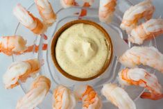 shrimp and dip in a glass bowl surrounded by small pieces of food on a plate