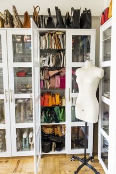 a white mannequin sitting in front of a closet filled with purses