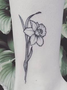 a flower tattoo on the ankle with leaves in the background and green plants behind it