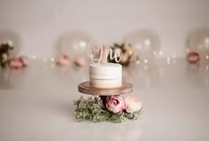 a white cake sitting on top of a wooden stand next to pink flowers and greenery