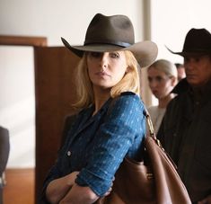 a woman wearing a cowboy hat and carrying a brown bag while standing next to other people