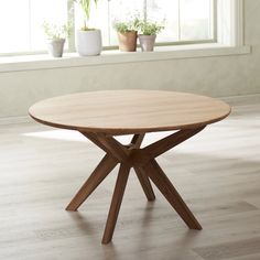 a round wooden table sitting on top of a hard wood floor next to a window