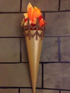 a gold cone shaped vase with flowers in it sitting on a brick wall next to a black tile floor