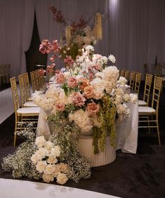 an arrangement of flowers and greenery on a table at a wedding reception with gold chairs