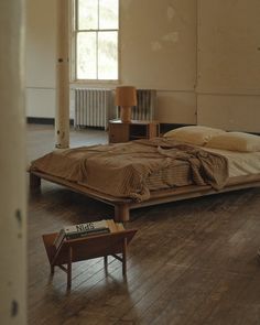 an empty bedroom with a bed, table and lamp on the floor in front of a window