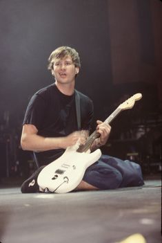 a man sitting on the ground playing an electric guitar