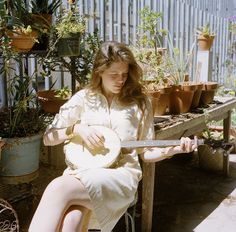 a woman is sitting on a bench with a guitar in her hand and potted plants behind her