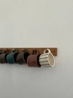 coffee mugs are lined up on a wooden rack with hooks for each one to hold them