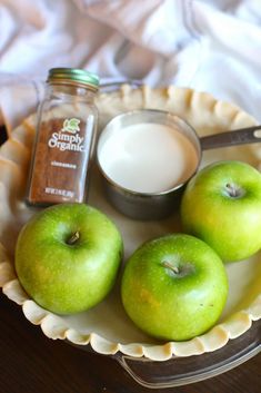 three green apples sitting on top of a white plate next to a jar of milk