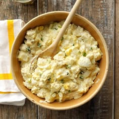 a bowl filled with mashed potatoes on top of a wooden table next to a spoon