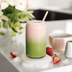 a green and pink drink sitting on top of a counter next to some strawberries