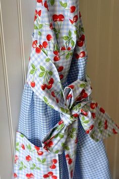 a blue and white checkered dress with cherries tied to the front, hanging on a hook