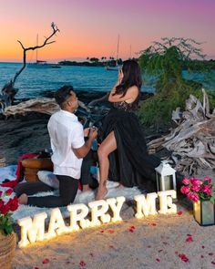 a man kneeling down next to a woman on the beach