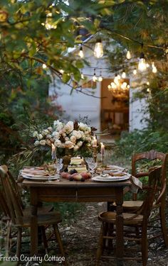 a table set for two with flowers and candles on it in the middle of a garden