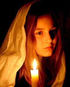 a woman holding a lit candle in her hand and wearing a nun's robe