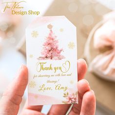 a person holding up a thank card with a pink christmas tree on the front and gold lettering