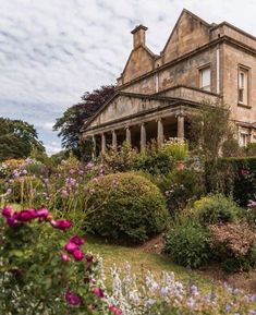 an old house surrounded by flowers and bushes