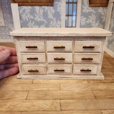 a hand holding a miniature white dresser with drawers