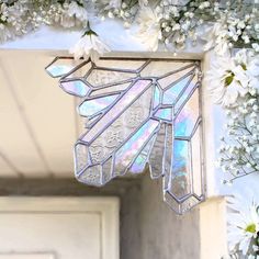 a stained glass window hanging from the side of a building with white flowers around it