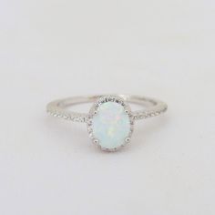 a white opal and diamond ring sitting on top of a table with a white background