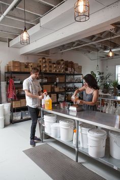 a man and woman standing at a counter in a room with lots of containers on it