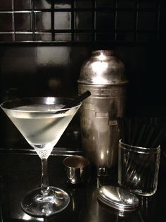 a martini sitting on top of a black counter next to a shaker and ice bucket