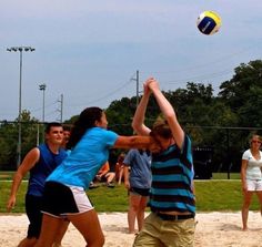 some people are playing volleyball in the sand and one is reaching up to hit the ball