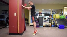 a man standing next to a red wall in a room filled with exercise balls and equipment