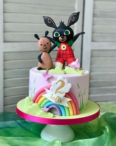 there is a cake with two small animals on it and rainbows in the background