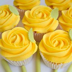 cupcakes with yellow frosting and green leaves on them are arranged in rows