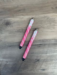 two pink and white pens sitting on top of a wooden table next to each other