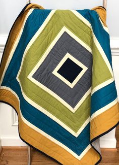 a green, blue and yellow quilt sitting on top of a wooden chair next to a white wall